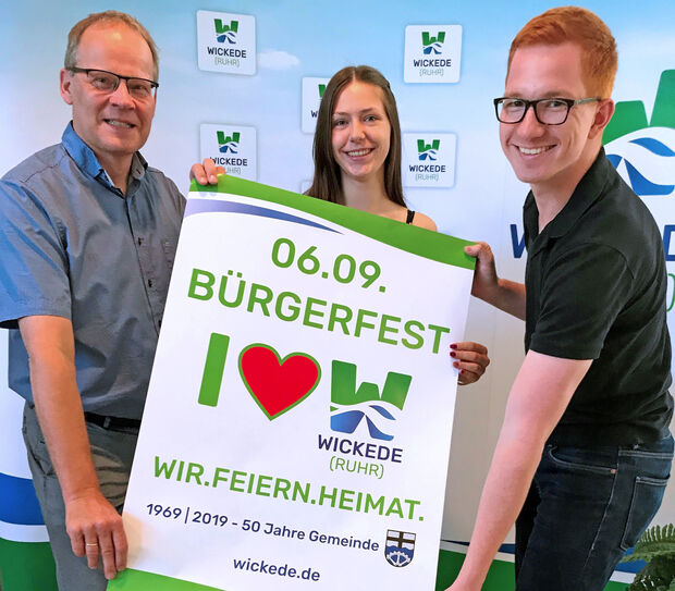 Die Gemeinde Wickede (Ruhr) lädt anlässlich ihres 50-jährigen Bestehens in diesem Jahr am Nachmittag und Abend des 6. September 2019 zum großen Bürgerfest auf den Marktplatz vor dem Rathaus ein. – Das Plakat zu dem Event präsentierten jetzt (von links): Bürgermeister Dr. Martin Michalzik (CDU), die neue Auszubildende Eva Brandl und Rathaus-Mitarbeiter David Schmeiser FOTO: GEMEINDE WICKEDE (RUHR) / MARION VOSS