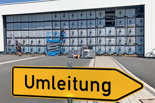 Für die Feier des Firmenjubiläums ist die Erlenstraße in Wickede an diesem Wochenende gesperrt. Aus riesigen Palettentanks hat man eine temporäre Wand in der Firmendurchfahrt errichtet. Die milchigen Kunststoffboxen werden für das Fest von hinten beleuchtet. FOTO: ANDREAS DUNKER
