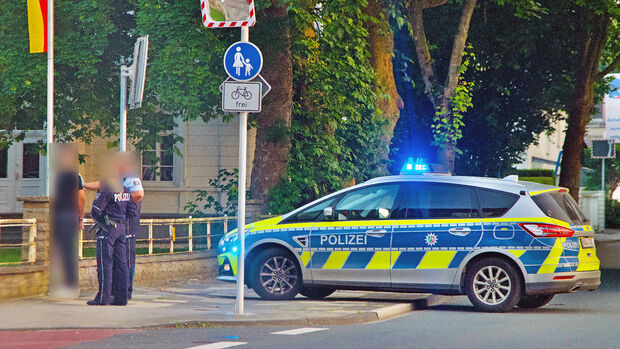 Die Polizei hält einen jungen Burschen fest, dem sie kurz zuvor offenbar Handfesseln angelegt hat. Der Streifenwagen steht quer auf Hauptstraße und Gehweg. FOTO: ANDREAS DUNKER